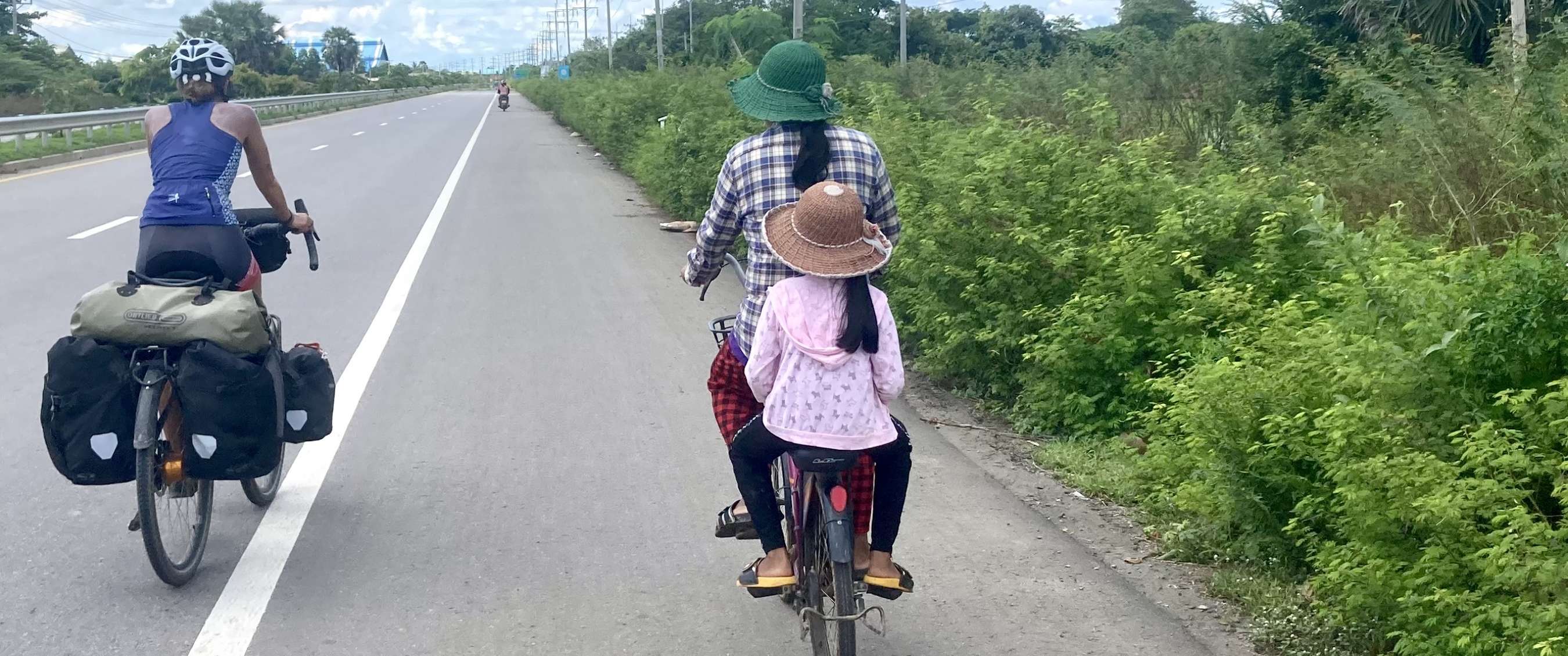 Fietstoerist met bepakking rijdt op een rustige weg in Azië naast een vrouw met een kind achterop de fiets.