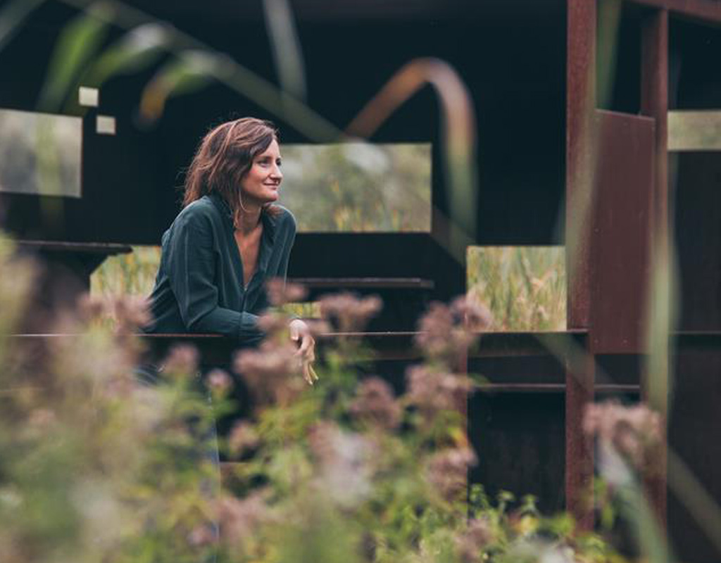 Claudia Verswyver geniet van het uitzicht bij een observatiepunt in een groen landschap.